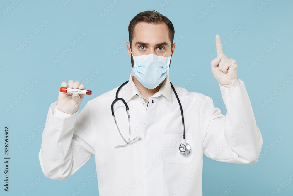 Male doctor man in gown face mask gloves isolated on blue background. Epidemic pandemic coronavirus 2019-ncov sars covid-19 flu virus concept. Hold blood test result Sample tube point index finger up.