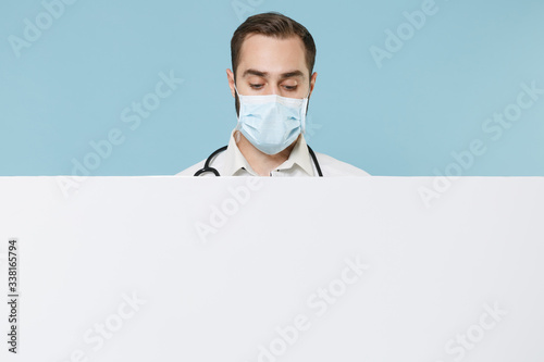 Male doctor man in gown sterile face mask isolated on blue background. Epidemic pandemic coronavirus 2019-ncov sars covid-19 flu virus. Hold big white empty blank billboard with place for text image. photo