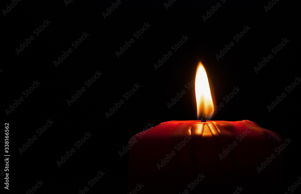 Candle lit. Beautiful red holiday candle, on a black background. Christmas, Easter. Candle lit. Beautiful red holiday candle, on a black background. Christmas, Easter.