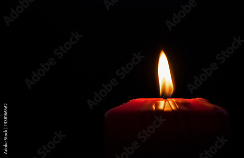 Candle lit. Beautiful red holiday candle, on a black background. Christmas, Easter.