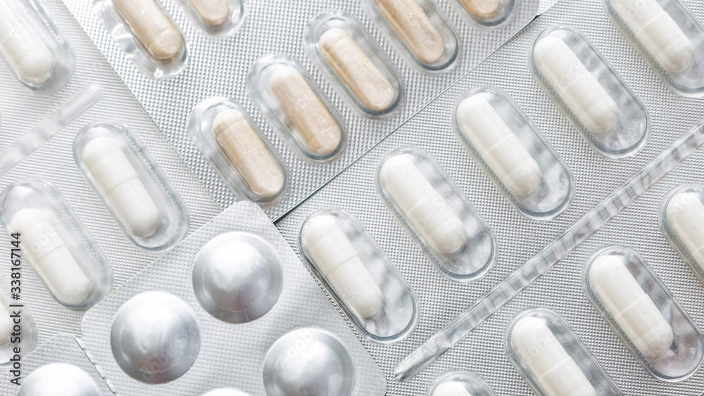 wide background, macro closeup of pills and white capsules, on a silver pharmaceutical blister pack wide background, macro closeup of pills and white capsules, on a silver pharmaceutical blister pack