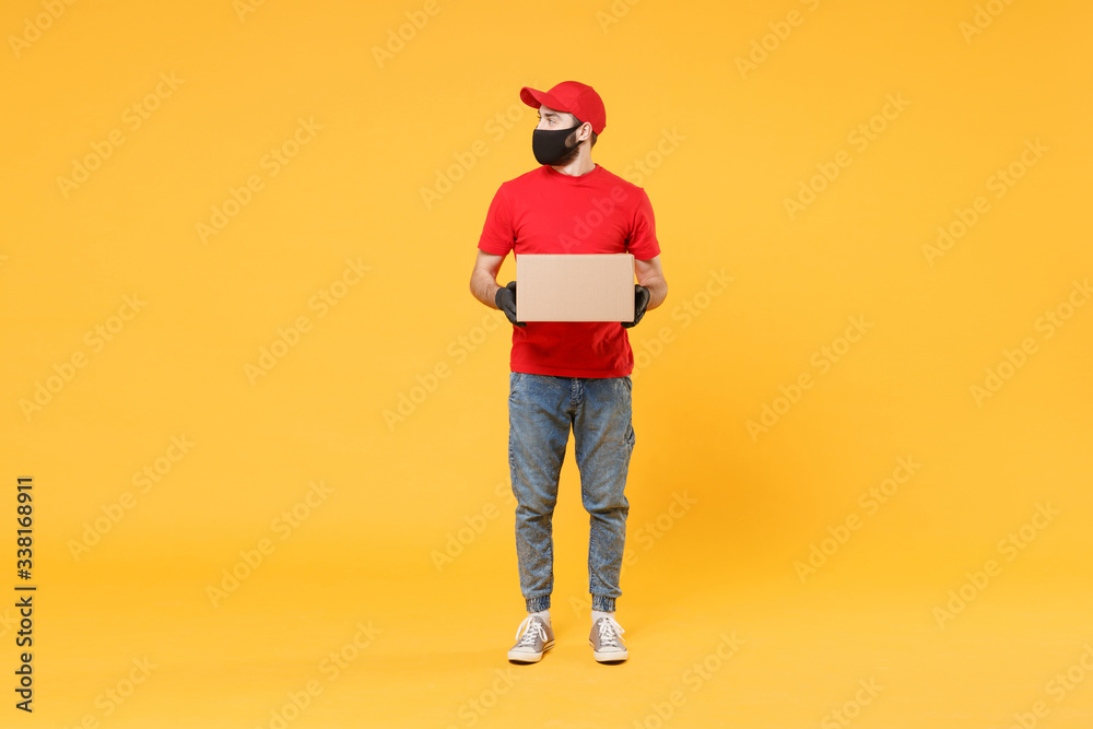 Delivery man employee in red cap blank t-shirt uniform face mask glove hold empty cardboard box isolated on yellow background studio Service quarantine pandemic coronavirus flu virus 2019-ncov concept Delivery man employee in red cap blank t-shirt uniform face mask glove hold empty cardboard box isolated on yellow background studio Service quarantine pandemic coronavirus flu virus 2019-ncov concept