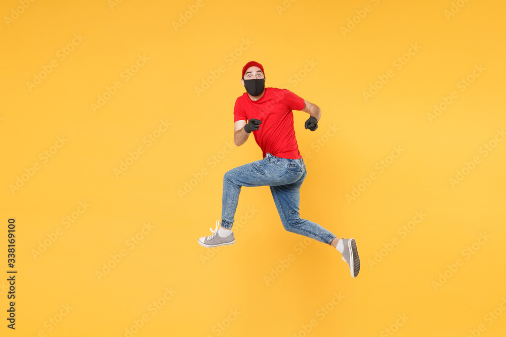 Fun jumping delivery man in red cap t-shirt uniform sterile face mask gloves isolated on yellow background studio Guy employee courier Service quarantine pandemic coronavirus virus 2019-ncov concept. Fun jumping delivery man in red cap t-shirt uniform sterile face mask gloves isolated on yellow background studio Guy employee courier Service quarantine pandemic coronavirus virus 2019-ncov concept.