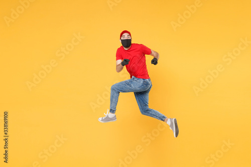 Fun jumping delivery man in red cap t-shirt uniform sterile face mask gloves isolated on yellow background studio Guy employee courier Service quarantine pandemic coronavirus virus 2019-ncov concept.