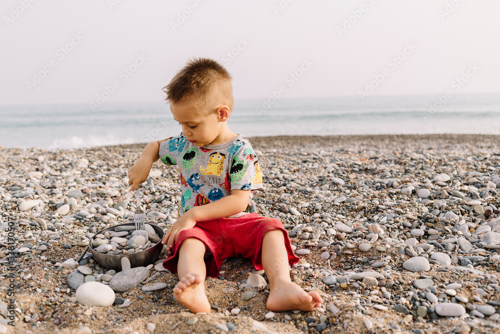 child on the beach plays with stones with a fork and a plate child on the beach plays with stones with a fork and a plate
