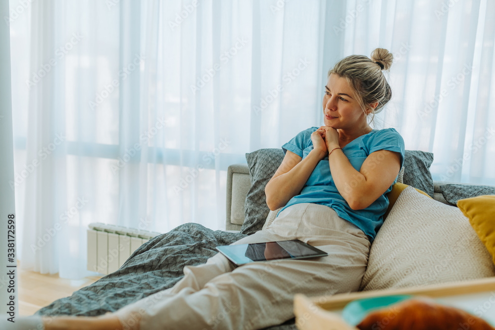 Photo of young woman in pajamas sitting on bed and thinking about her loving person. Young woman is sitting on bed with tablet computer in her lap while enjoying free morning. Photo of young woman in pajamas sitting on bed and thinking about her loving person. Young woman is sitting on bed with tablet computer in her lap while enjoying free morning.