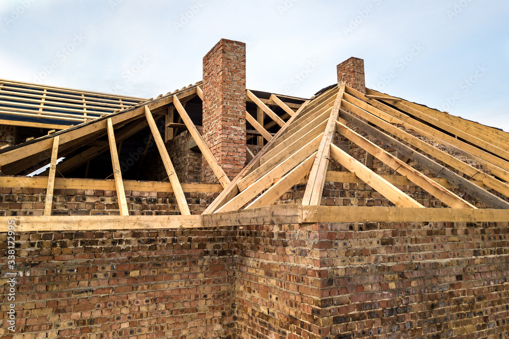 Private residential house with wooden roof frame structure under construction. Unfinished brick building under development.