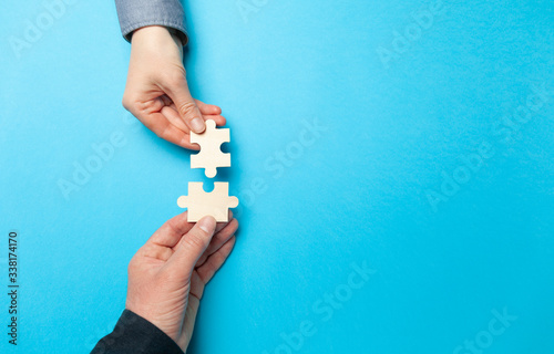 Two hands connect puzzles on a blue background. Cooperation and teamwork in business. Collaboration people for success.