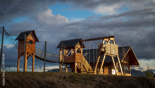 Frog view of wooden Children playground. Houses and other object for children to play with lit by sun and majestic cloudy backdrop. © Anze