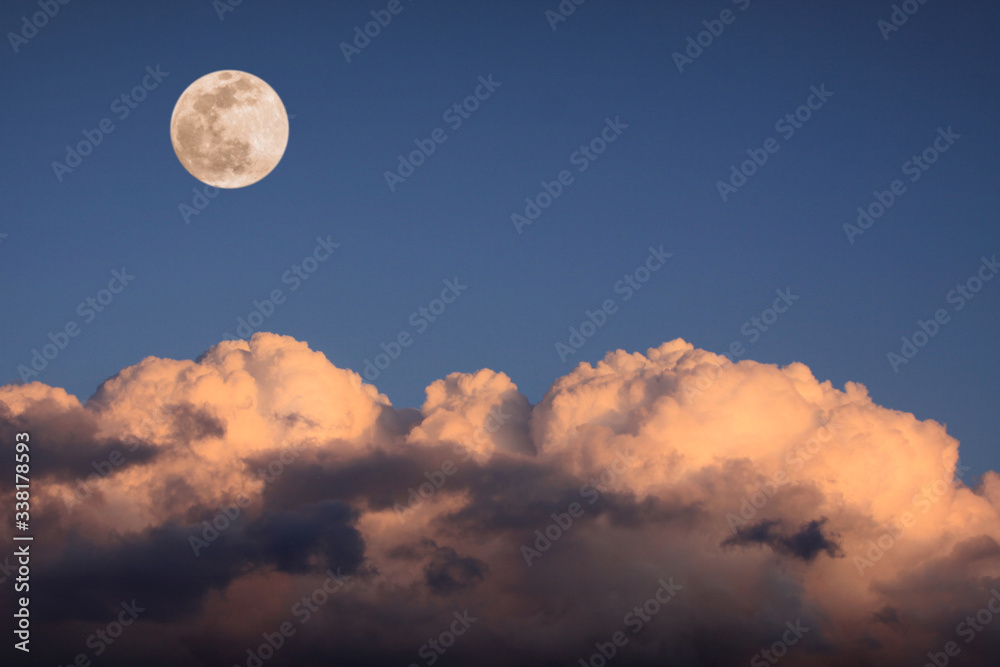 bright full moon over thick puffy white clouds at sunset bright full moon over thick puffy white clouds at sunset
