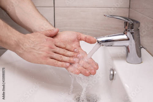 A man carefully washes his hands with water under the tap in the bathroom