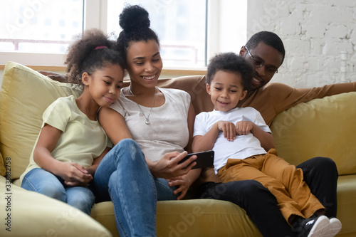 African american smiling family with two children having good time using smartphone. Young happy diverse husband and wife with cute daughter and son using applications in mobile phone.