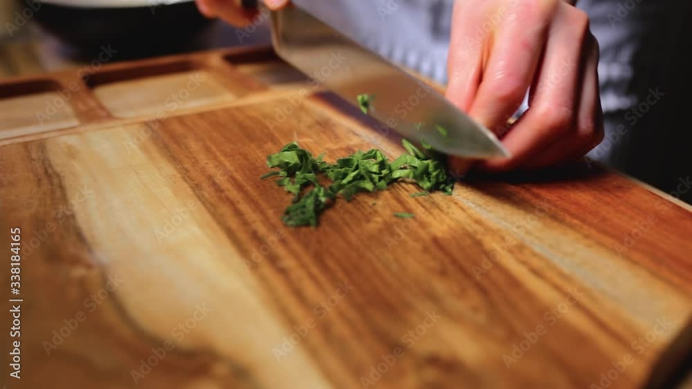 A woman hand chopping with a knife spinach/greens on cutting board A woman hand chopping with a knife spinach/greens on cutting board