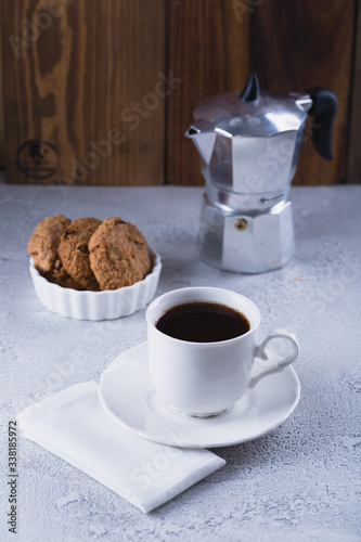 White cup of coffee with oatmeal cookies and coffee maker, breakfast concept, selective focus