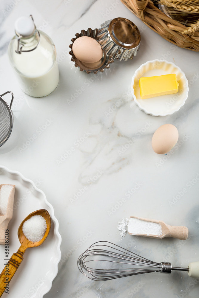 Ingredients for sweet baking on white marble background, eggs, milk jar, sugar, flour, butter, baking powder. Cookies or cake baking praparation. White round mock up for text in the center, copy space Ingredients for sweet baking on white marble background, eggs, milk jar, sugar, flour, butter, baking powder. Cookies or cake baking praparation. White round mock up for text in the center, copy space