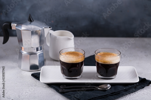 Two cups of fresh espresso on white rectangular tray with milk jar and coffee maker. Horisontal view, copy space, breakfast concept 