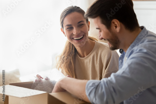 Excited young married couple homeowners chatting, unpacking belongings after moving in new house apartment. Happy family spouses unboxing delivered items from internet store, satisfied with purchase.