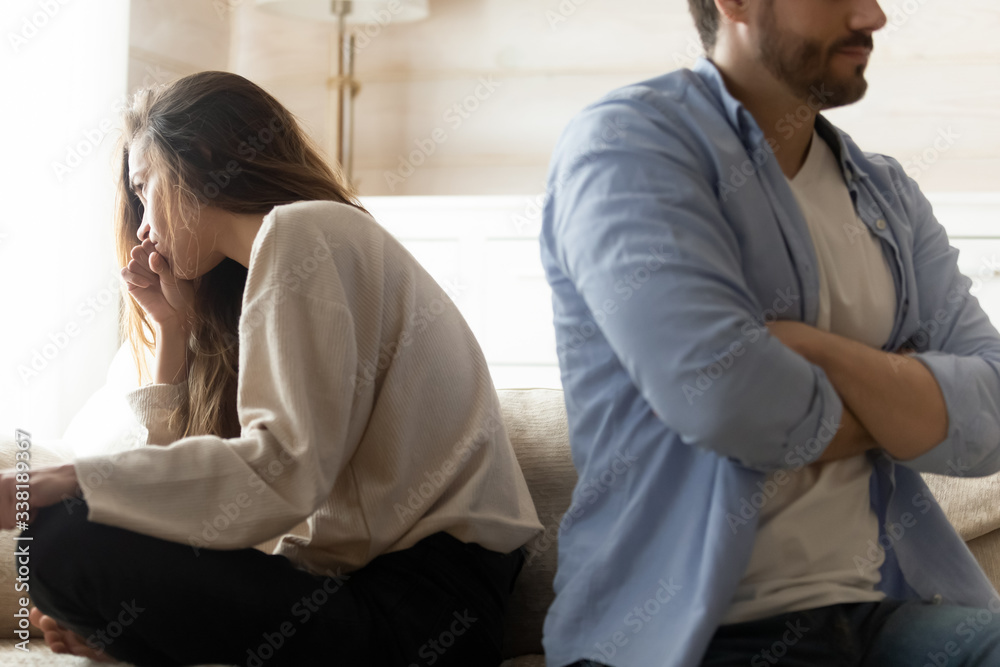 Stressed young married couple sitting separately on different sides of sofa, ignoring each other after quarrel. Offended spouses do not talk communicate, feeling depressed disappointed after argue. Stressed young married couple sitting separately on different sides of sofa, ignoring each other after quarrel. Offended spouses do not talk communicate, feeling depressed disappointed after argue.