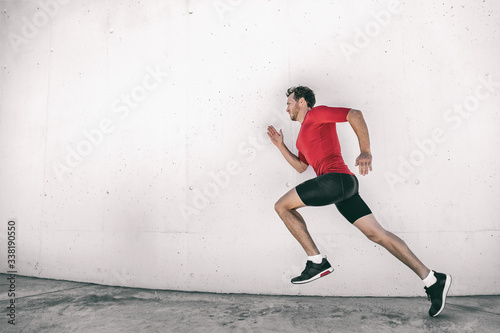 Running man fit athlete male runner working out outside doing city street run sprinting along gym wall. Sprinter going fast living active lifestyle doing sprint hiit high intensity interval training.