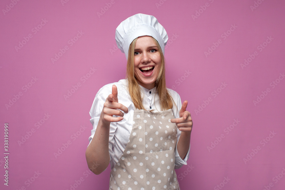 young cheerful girl cook in kitchen clothes shows fingers to the camera and smiles on a colored background, woman housewife makes a gesture with her hands young cheerful girl cook in kitchen clothes shows fingers to the camera and smiles on a colored background, woman housewife makes a gesture with her hands