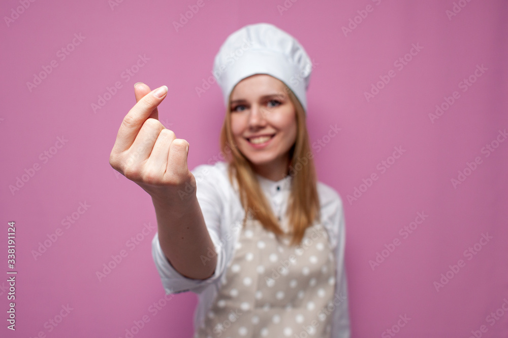 cheerful girl cook in kitchen clothes shows italian heart sign and smiles on a colored background, woman housewife makes hand gesture cheerful girl cook in kitchen clothes shows italian heart sign and smiles on a colored background, woman housewife makes hand gesture