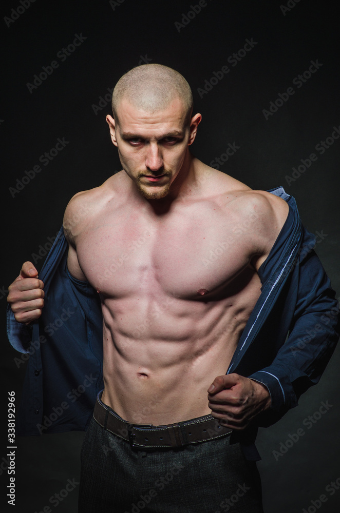 A stylish, bald young man stands with a naked torso on a dark background in the category