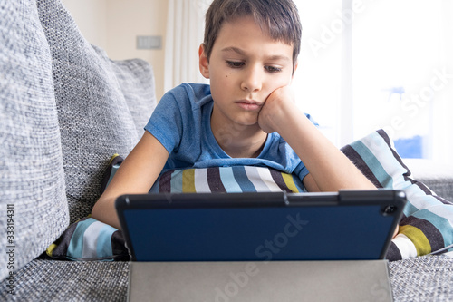 Boy lying on sofa with digital tablet computer at home. Technology, ditance education, online learning, playing games concept photo