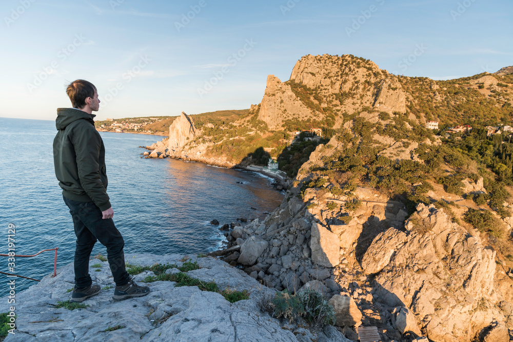 Portrait of a young man against the background of the sea. Tourist guy with a backpack on the background of the water and the panorama of the beach.