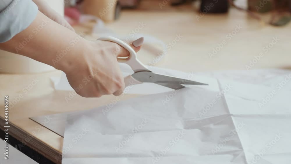 Close up shot of hands of unrecognizable female florist cutting craft paper with scissors while working at table in flower shop