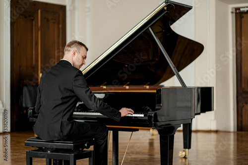 young handsome caucasian man in formal elegant suit gracefully play piano. professional pianist perform classic music photo