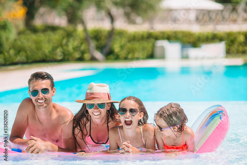 Happy family of four in outdoors swimming pool