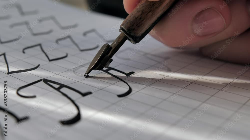 Calligraphy on sun light. Writing with nib fountain pen, black ink on white paper. Capital letter A. Cinematic close-up.