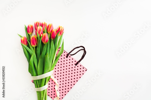 Fototapeta Naklejka Na Ścianę i Meble -  Beautiful spring bouquet of pink tulips flowers with holiday package white ribbon and on white. Flat lay. Copy space