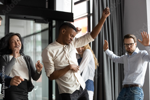 Excited happy multiracial businesspeople have fun engaged in activity in office together, overjoyed diverse colleagues dance celebrate successful business project, Friday celebration concept