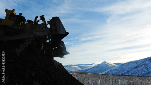 Yellow bulldozer on a construction site overlooking mountain and sky © Aliaksei
