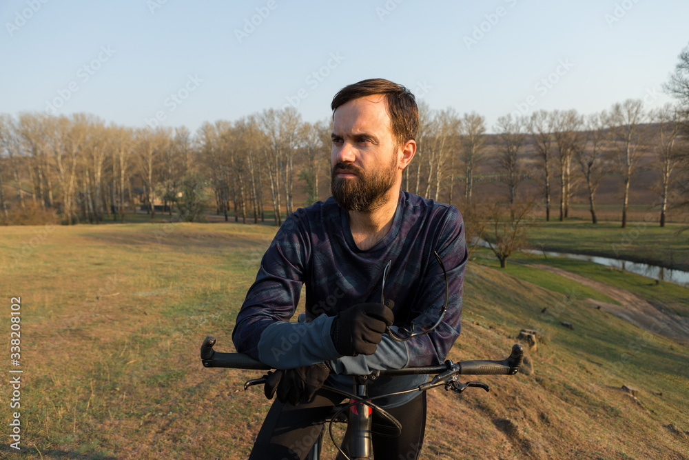 Fototapeta premium Cyclist in shorts and jersey on a modern carbon hardtail bike with an air suspension fork standing on a cliff against the background of fresh green spring forest