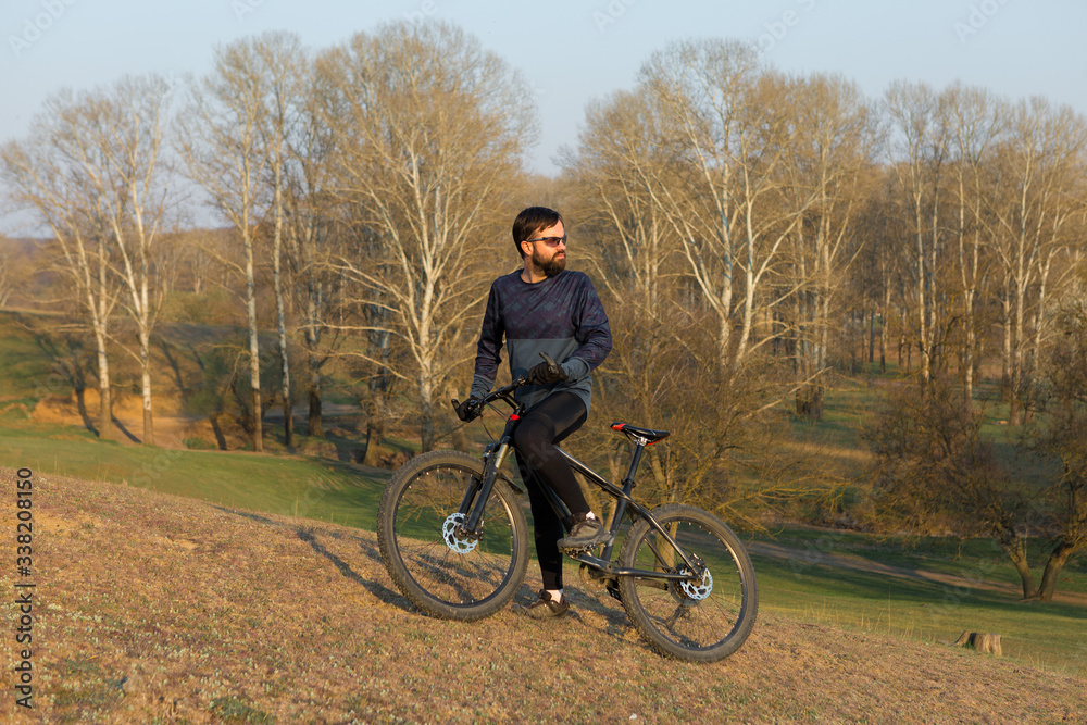 Fototapeta premium Cyclist in shorts and jersey on a modern carbon hardtail bike with an air suspension fork standing on a cliff against the background of fresh green spring forest