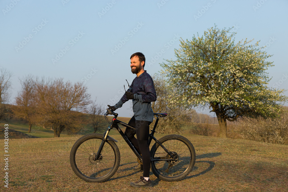 Cyclist in shorts and jersey on a modern carbon hardtail bike with an air suspension fork standing on a cliff against the background of fresh green spring forest