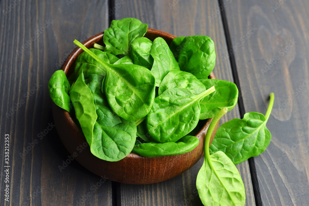 Spinach leaves in wooden bowl on dark background. Vegan food lifestyle concept. Spinach leaves in wooden bowl on dark background. Vegan food lifestyle concept.