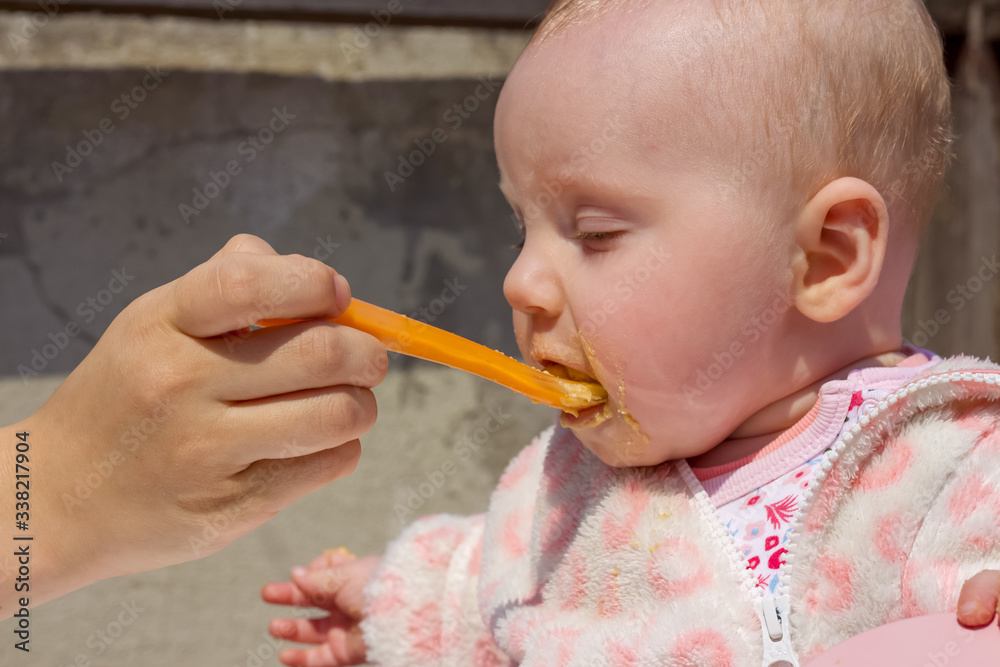 Mom feeding her little cute blonde baby girl with her baby's favorite food and baby's mouth is dirty,supplementary food Mom feeding her little cute blonde baby girl with her baby's favorite food and baby's mouth is dirty,supplementary food