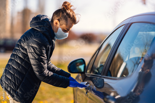 Woman wearing protection face mask and protective gloves disinfecting the car with antibacterial wet wipes.