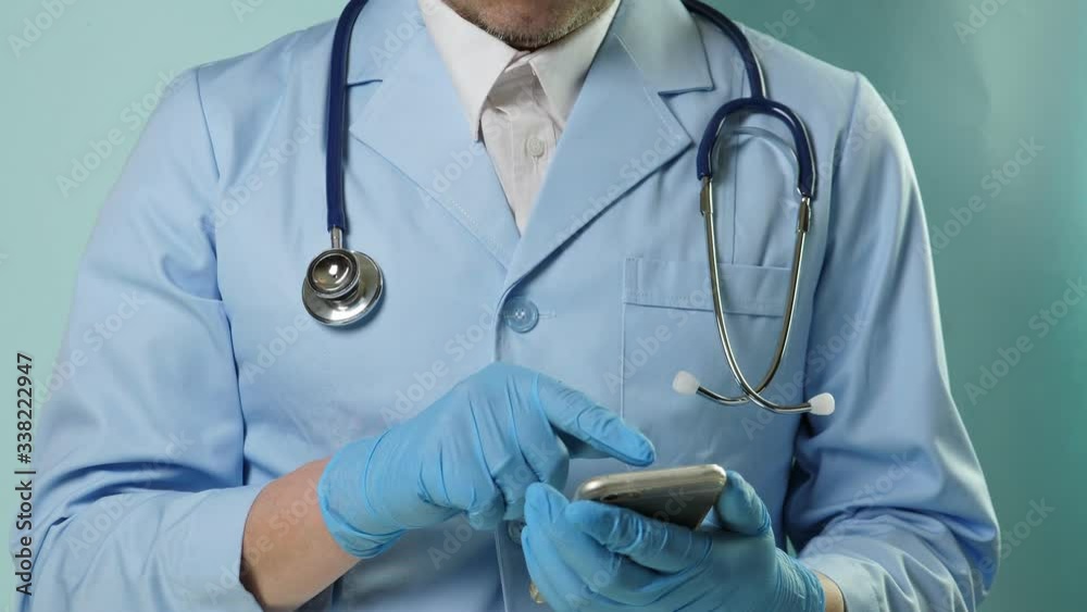 Doctor in professional medical suit and blue gloves use smartphone. No face Doctor in professional medical suit and blue gloves use smartphone. No face