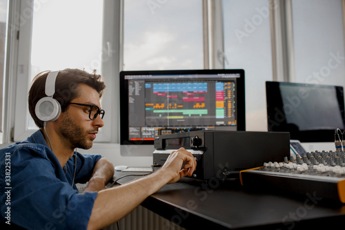 Male music arranger works with sound amplifier he is composing song on midi piano and audio equipment in digital recording studio. DJ in broadcasting studio. music, technology and equipment concept.