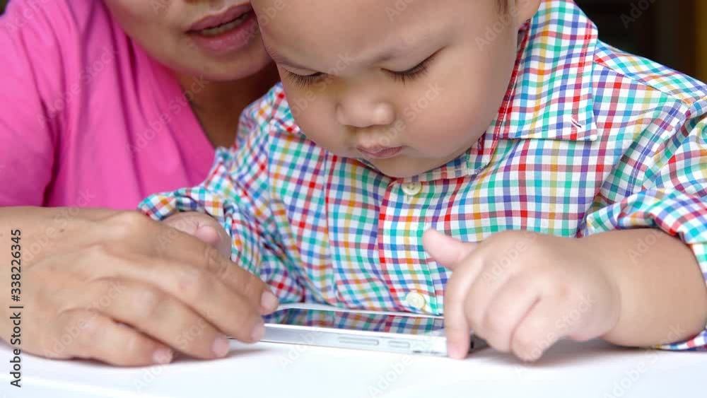Little boy having fun with mom enjoy using looking at mobile screen learning from content in smartphone Little boy having fun with mom enjoy using looking at mobile screen learning from content in smartphone