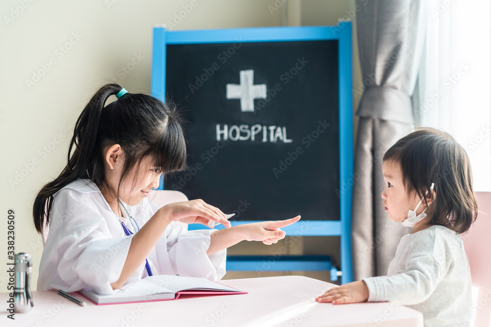 Two Asian cute girls pretend to be doctor and patient. Young doctor check fever temperature by using thermometer of sick baby who wear mask at hospital. Doctor diagnose disease and give some advice Two Asian cute girls pretend to be doctor and patient. Young doctor check fever temperature by using thermometer of sick baby who wear mask at hospital. Doctor diagnose disease and give some advice
