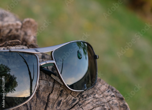anteojos de sol con una gota de agua encima posado en tronco de madera