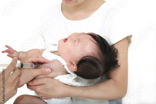 母に抱かれたまま、注射を打たれ泣く赤ちゃん。