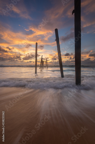 sea waves lash line impact on the sand beach with old wood bridge at sunset, pilai beach, phang nga , Thailand photo