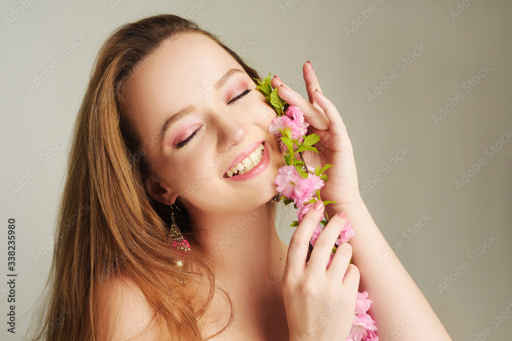Girl with inflorescences, spring, portrait, beautiful model with a pink flower, sprouts, buds. The girl inherits the beginning of spring. Delicate pink makeup inspired by flowers and spring.