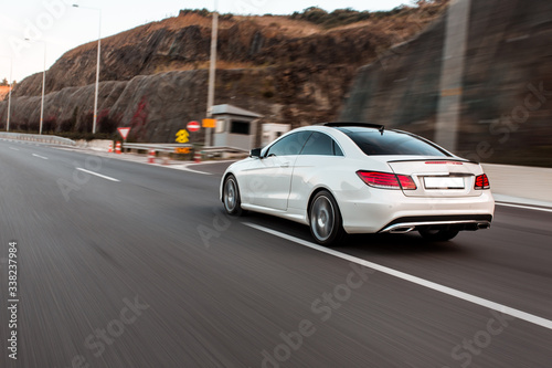 White business class sedan car driving on the highway across green hills